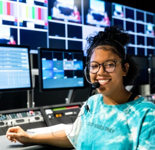 A student wearing a blue shirt sits at a TV studio control panel in the RTF program at ACC.