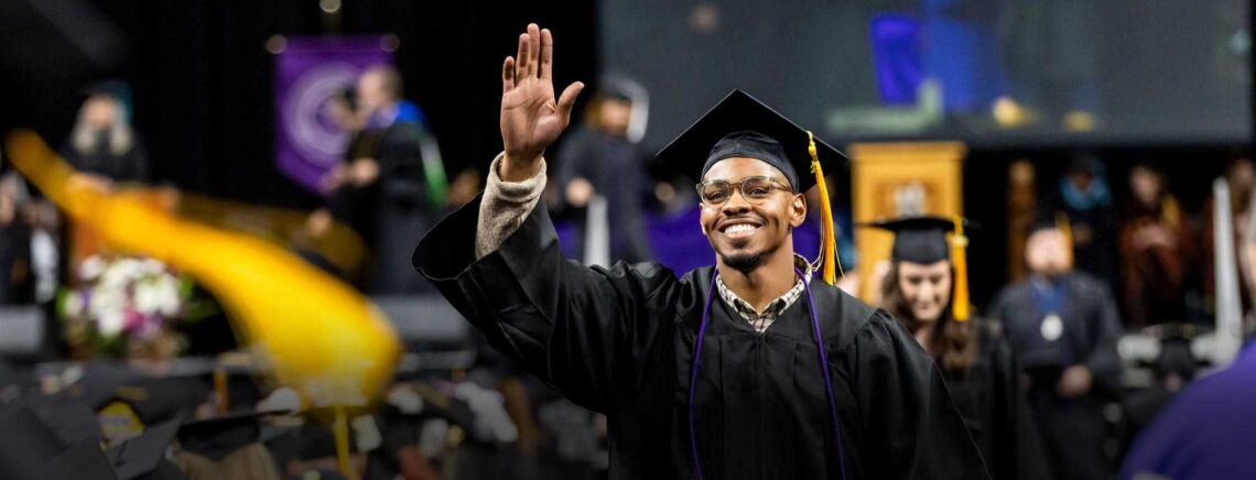 An African-American ACC student smiles and waves as he walks toward his seat after crossing the stage during the commencement ceremony.