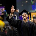 An African-American ACC student smiles and waves as he walks toward his seat after crossing the stage during the commencement ceremony.