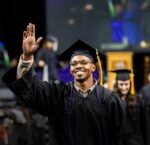 An African-American ACC student smiles and waves as he walks toward his seat after crossing the stage during the commencement ceremony.