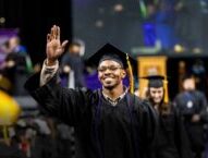 An African-American ACC student smiles and waves as he walks toward his seat after crossing the stage during the commencement ceremony.